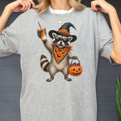 May include: A heather gray t-shirt featuring a graphic of a raccoon wearing a black witch hat with a pumpkin, heart-shaped sunglasses, and an orange bandana with a bat pattern. The raccoon holds an iced coffee and an orange jack-o'-lantern bucket.