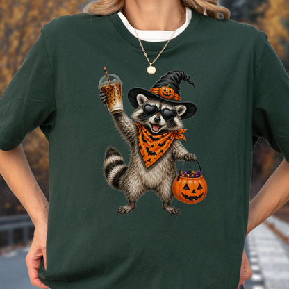 May include: A dark green t-shirt featuring a graphic of a raccoon wearing a black witch hat with a small pumpkin, heart-shaped sunglasses, and an orange bandana with black bats. The raccoon holds an iced coffee and a jack-o'-lantern candy bucket.