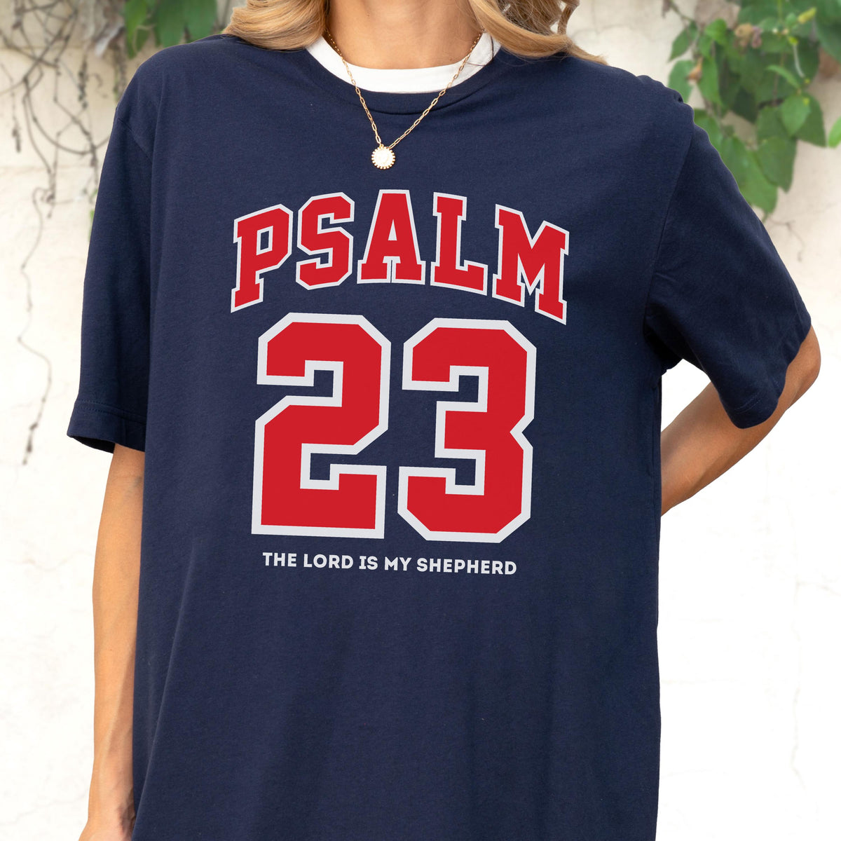 May include: A navy blue short-sleeve t-shirt featuring the red text PSALM 23 in a collegiate font, with the number 23 in large red block lettering below it, and the white text THE LORD IS MY SHEPHERD printed in a smaller font at the bottom.