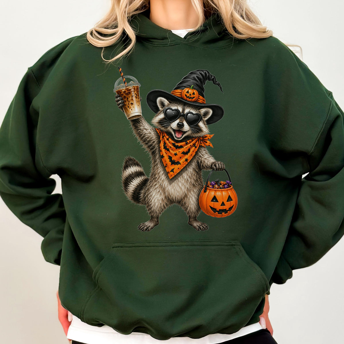 May include: A dark green hooded sweatshirt featuring a graphic of a raccoon wearing a black witch hat with a pumpkin, heart-shaped sunglasses, and an orange bat-patterned bandana. The raccoon holds a plastic cup and a jack-o'-lantern candy bucket.
