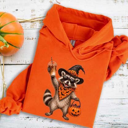 May include: An orange hooded sweatshirt featuring a graphic of a raccoon wearing a witch hat with a pumpkin, heart-shaped sunglasses, and an orange bandana with black bats. The raccoon holds an iced coffee and a jack-o'-lantern candy bucket.