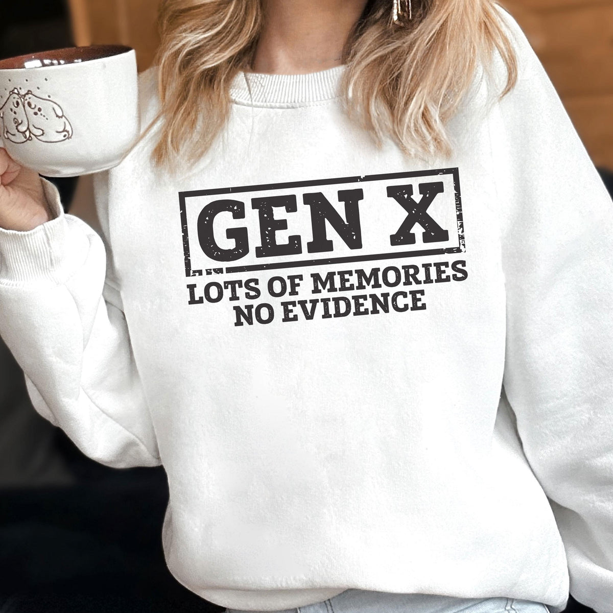 May include: A white crewneck sweatshirt featuring a black graphic print that reads GEN X in a rectangular border, with the text LOTS OF MEMORIES NO EVIDENCE underneath. The design has a distressed, weathered texture throughout the lettering.