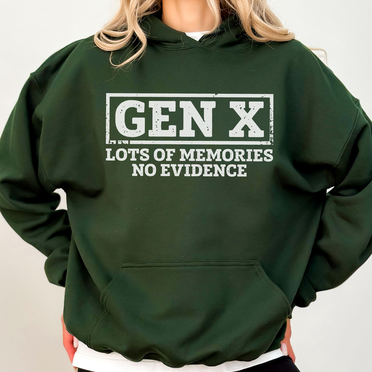 May include: A dark forest green hooded sweatshirt featuring a white graphic print on the chest. The text reads GEN X in a rectangular border, followed by the words LOTS OF MEMORIES NO EVIDENCE. The hoodie includes a front kangaroo pocket.