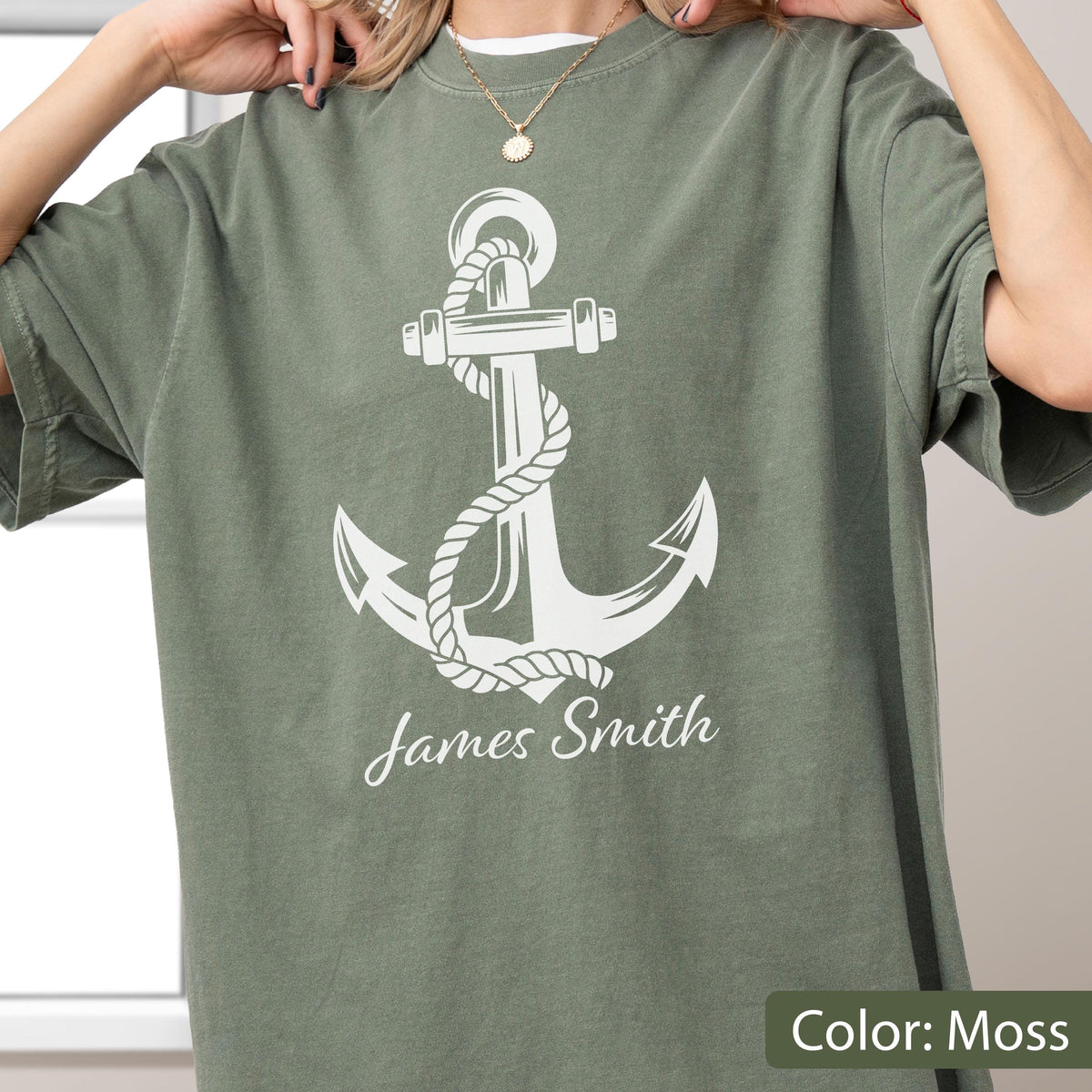 May include: A moss green short-sleeve t-shirt featuring a large white graphic of a nautical anchor wrapped in rope. Below the anchor, the name James Smith is printed in a white script font. The shirt has a crew neckline and a relaxed fit.