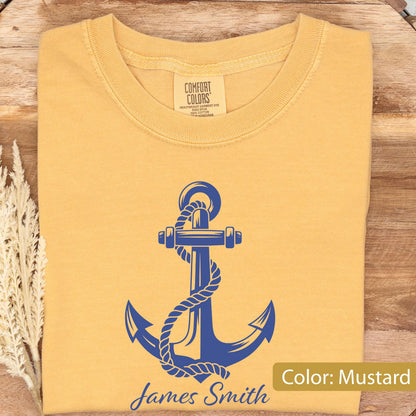 May include: A mustard yellow t-shirt featuring a blue graphic of a nautical anchor wrapped in rope. The shirt has a crew neckline and a Comfort Colors brand label at the inner collar. The text James Smith is printed in blue below the anchor.