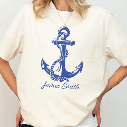 May include: A cream-colored short-sleeve t-shirt featuring a large blue graphic of a nautical anchor wrapped in a rope. Below the anchor, the name James Smith is printed in a blue script font. The shirt has a crew neckline and short sleeves.