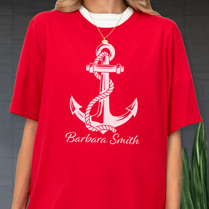 May include: A bright red short-sleeved t-shirt featuring a large white graphic of a nautical anchor wrapped in a rope. Below the anchor, the name Barbara Smith is printed in a white cursive script font. A thin gold chain necklace is visible.