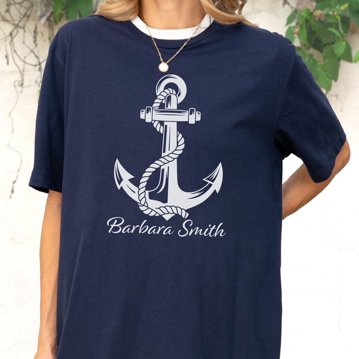 May include: A navy blue short-sleeved t-shirt featuring a large white graphic of a nautical anchor wrapped in rope. Below the anchor, the name Barbara Smith is printed in a white cursive script font. The shirt has a crew neckline and a simple design.