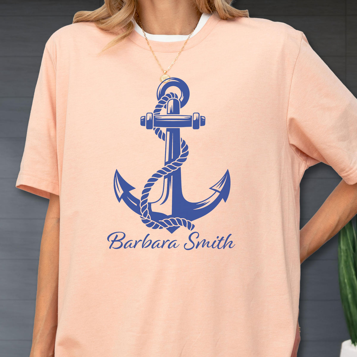 May include: A peach-colored short-sleeve t-shirt featuring a large blue graphic of a nautical anchor wrapped in rope. Below the anchor, the text "Barbara Smith" is printed in a blue cursive script font across the center of the chest.