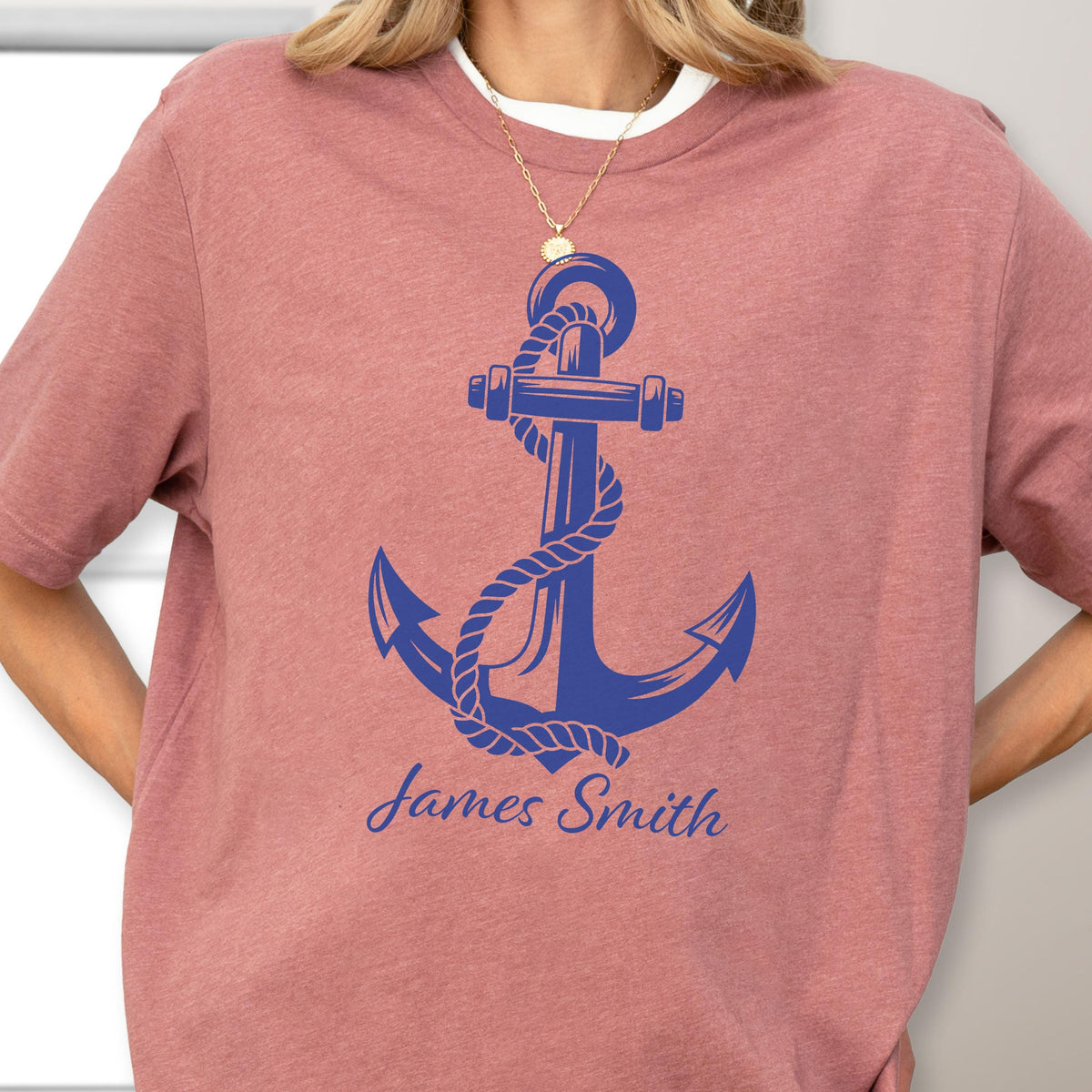 May include: A dusty rose short-sleeve t-shirt featuring a large blue graphic of a nautical anchor wrapped in rope. Below the anchor, the name James Smith is printed in a blue script font. The shirt has a crew neckline and a heathered texture.