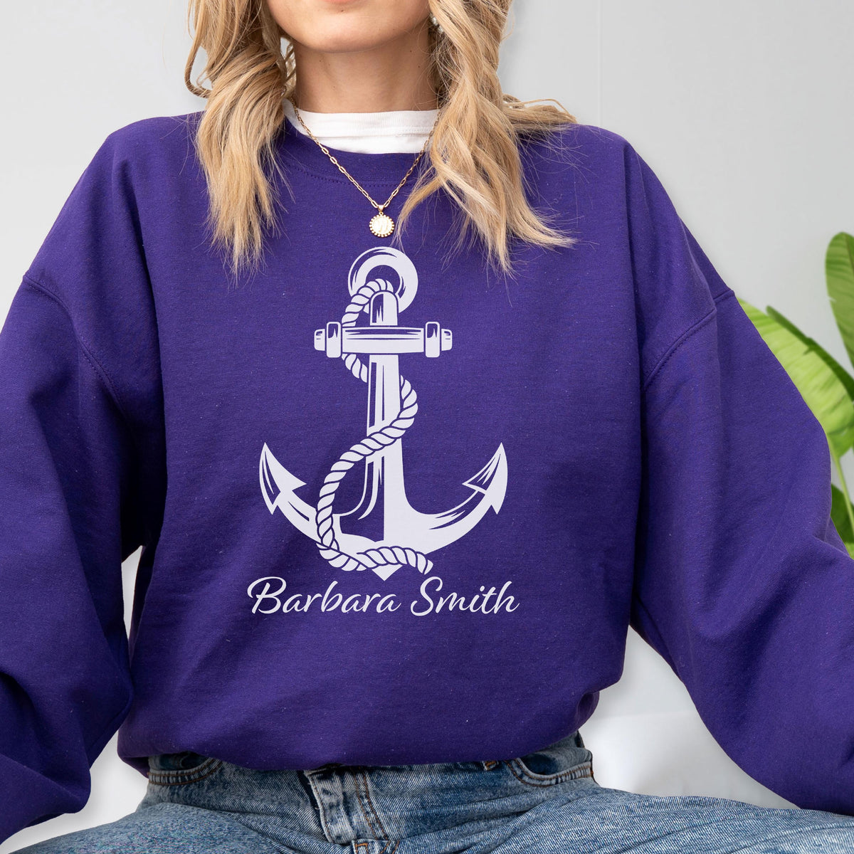 May include: A deep purple long-sleeve crewneck sweatshirt featuring a large white graphic of a nautical anchor wrapped in rope. The text "Barbara Smith" is printed in a white script font directly below the anchor design on the front.