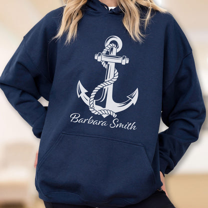 May include: A navy blue hooded sweatshirt featuring a large white graphic of a nautical anchor wrapped in rope. Below the anchor, the name Barbara Smith is printed in a white cursive script font. The garment includes a front kangaroo pocket.
