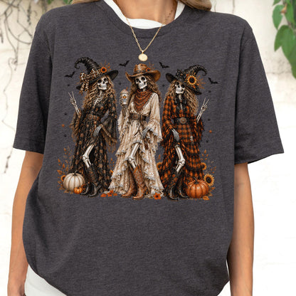 May include: A dark charcoal gray t-shirt featuring a graphic print of three skeletons dressed in western-style clothing, including hats, long dresses, and boots. The skeletons are surrounded by sunflowers, pumpkins, and small bats on a dark background.
