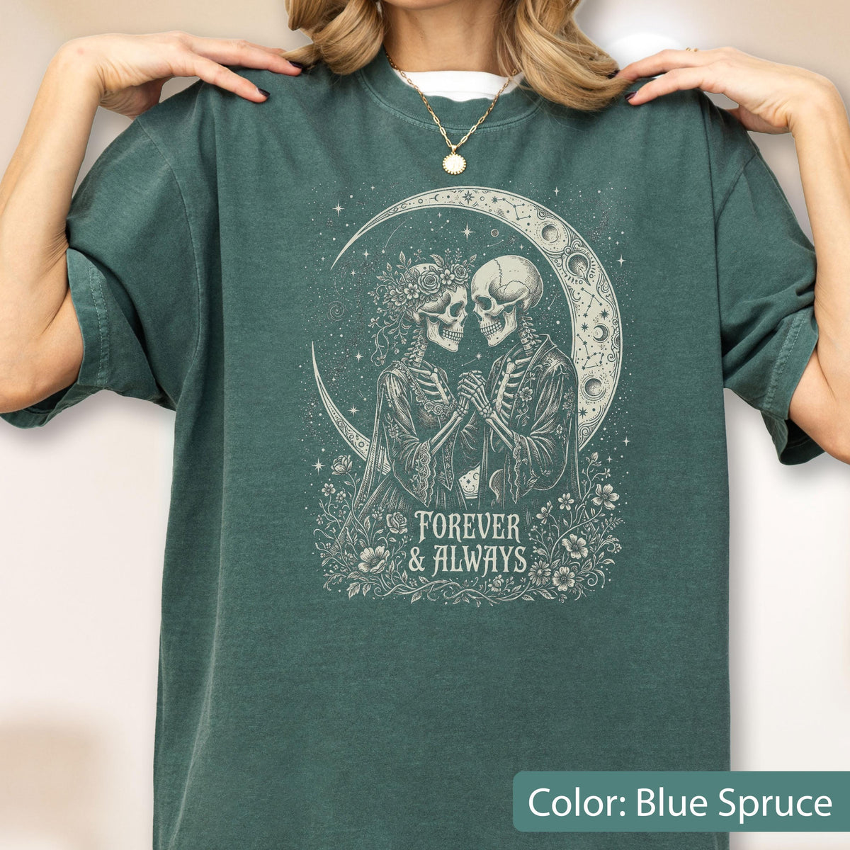 May include: A blue spruce t-shirt featuring a graphic print of two skeletons holding hands under a crescent moon. The design includes floral elements and the text "FOREVER & ALWAYS" in a decorative font. The shirt has short sleeves and a crew neck.