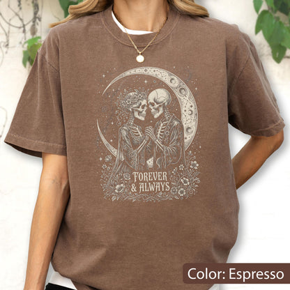 May include: An espresso brown short-sleeve t-shirt featuring a cream-colored graphic of two skeletons holding hands under a crescent moon. The design includes floral accents and the text "FOREVER & ALWAYS" printed in a serif font below the skeletons.
