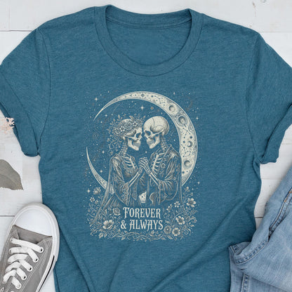 May include: A teal short-sleeve t-shirt featuring a graphic print of two skeletons holding hands in front of a crescent moon. The design includes floral accents and the text "FOREVER & ALWAYS" in a decorative font centered below the skeletons.
