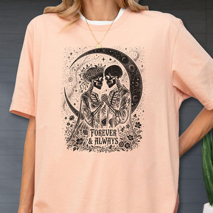 May include: A peach-colored t-shirt featuring a black graphic print of two skeletons holding hands under a crescent moon. The design includes floral accents and the text "FOREVER & ALWAYS" centered below the figures in a decorative serif font.