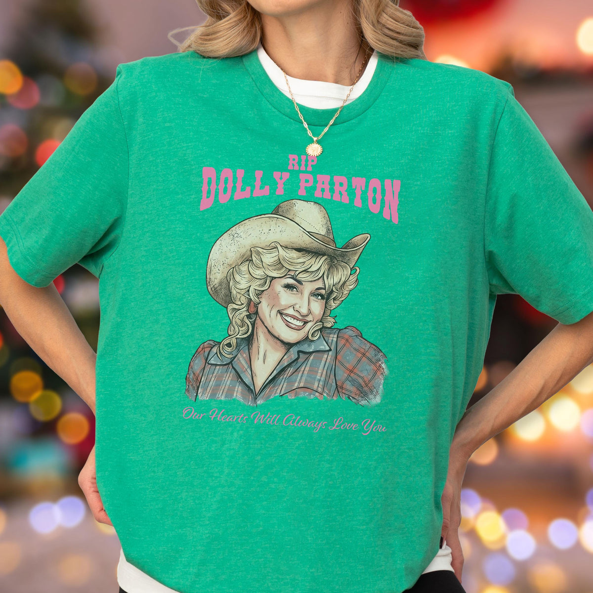 May include: A bright green short-sleeved t-shirt featuring a graphic illustration of Dolly Parton wearing a cowboy hat and a plaid shirt. The text reads RIP DOLLY PARTON in pink letters above the portrait and Our Hearts Will Always Love You below.