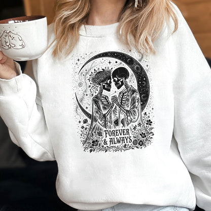 May include: A white crewneck sweatshirt featuring a black graphic print of two skeletons holding hands in front of a crescent moon. The design includes floral accents and the text Forever & Always. A white mug with a small black line drawing is visible.