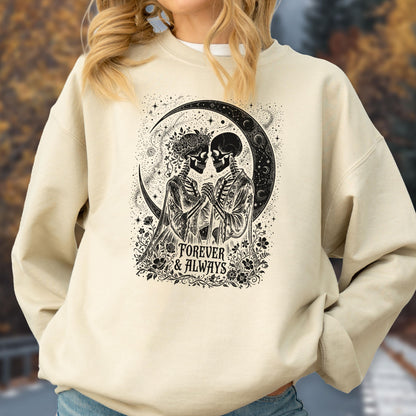 May include: A beige crewneck sweatshirt featuring a black graphic print of two skeletons holding hands under a crescent moon. The design includes floral accents and the text "FOREVER & ALWAYS" centered at the bottom of the illustration.