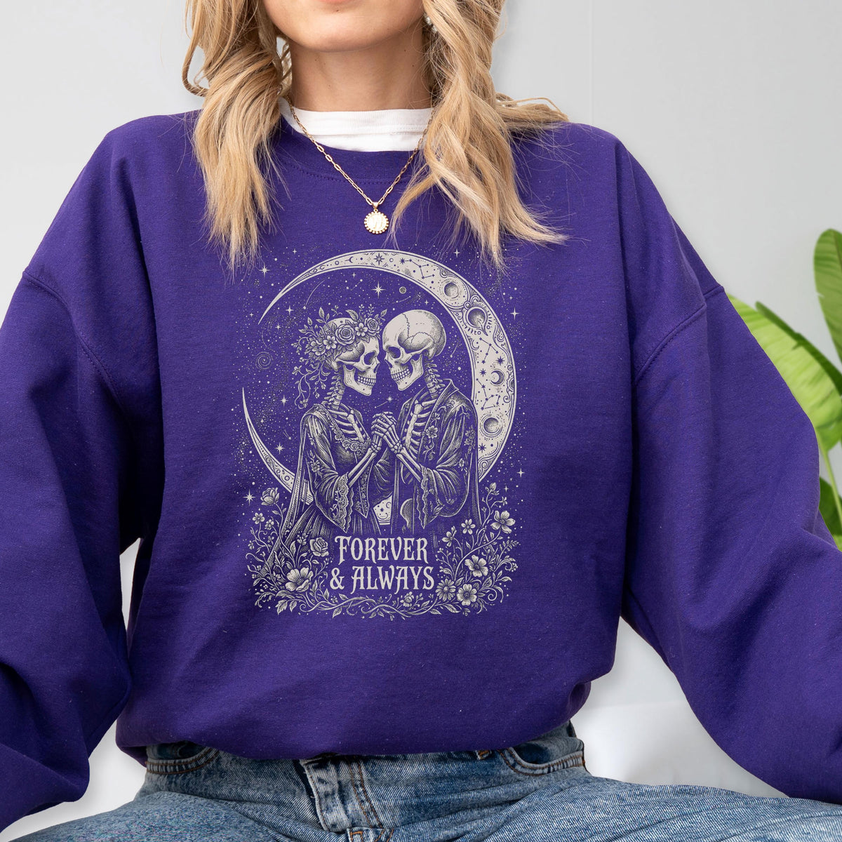 May include: A deep purple long-sleeve sweatshirt featuring a white graphic print of two skeletons holding hands under a crescent moon. The design includes floral accents and the text "FOREVER & ALWAYS" centered below the skeletons, set against a dark background.