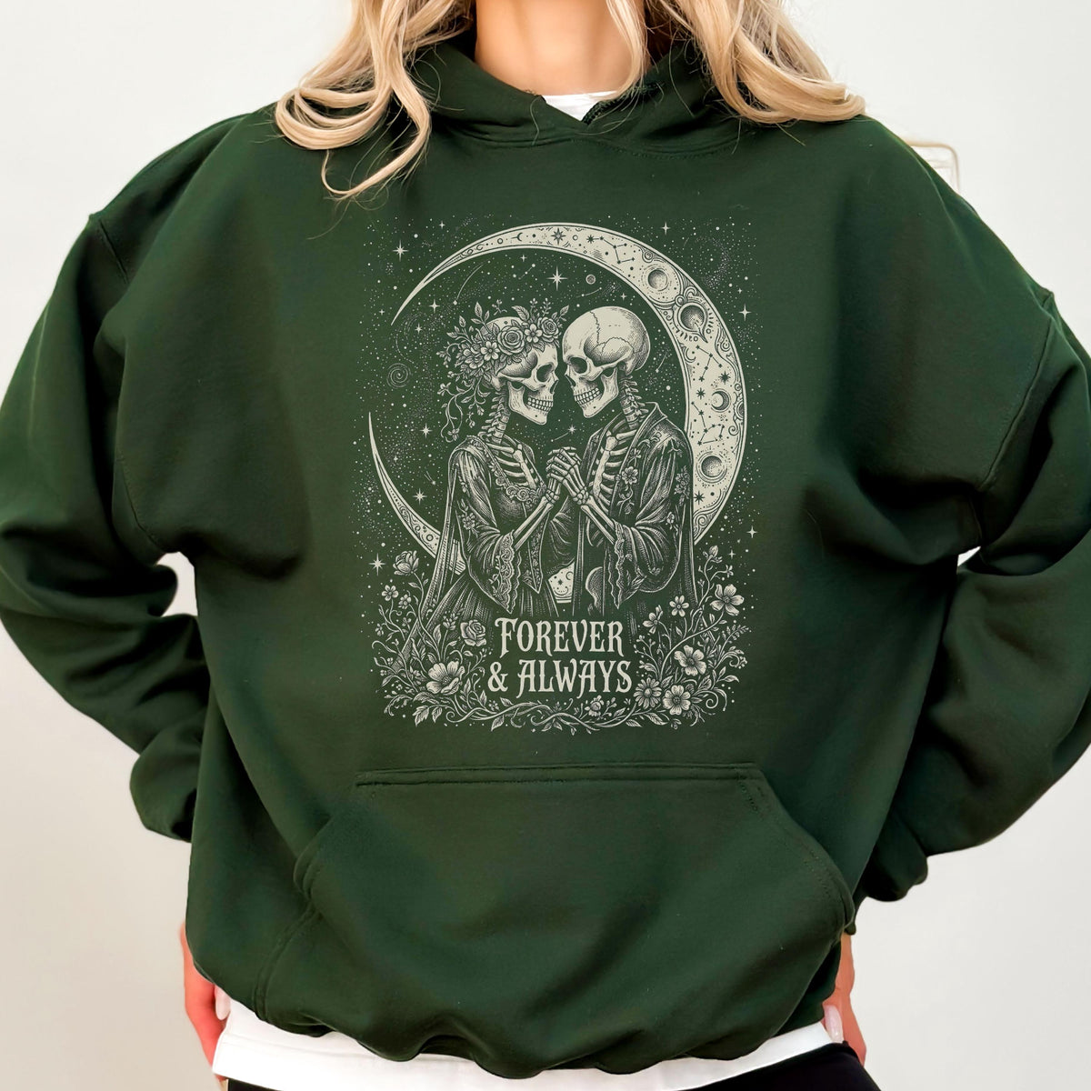May include: A dark forest green hooded sweatshirt featuring a graphic print of two skeletons holding hands under a crescent moon. The design includes floral elements and the text "FOREVER & ALWAYS" printed in a decorative font below the figures.