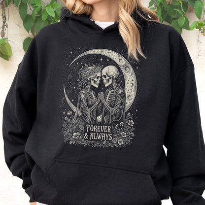 May include: A black hooded sweatshirt featuring a graphic print of two skeletons holding hands in front of a crescent moon. The design includes floral accents and the text "FOREVER & ALWAYS" in a decorative font, centered on the chest area.