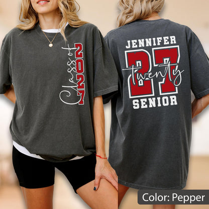 May include: A charcoal gray short-sleeve t-shirt featuring white and red graphics. The front displays "Class of 2027" vertically. The back shows the name "JENNIFER" above a large red "27" with the word "twenty" in script and "SENIOR" below.
