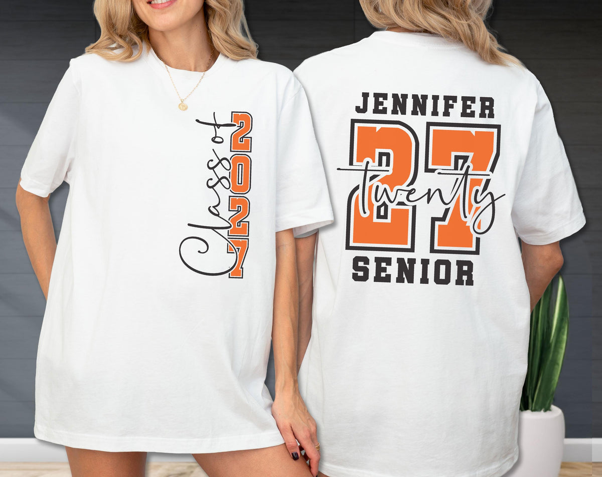 May include: A white t-shirt featuring a graphic design on the front and back. The front displays the text "Class of 2027" in black and orange. The back features the name "JENNIFER" above the number "27" in orange, with "twenty" and "SENIOR" text.