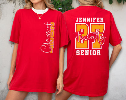 May include: A red short-sleeve t-shirt featuring white and yellow graphic text. The front displays vertical text reading Class of 2027. The back features the name Jennifer, the number 27, the word twenty in script, and the word Senior in block letters.
