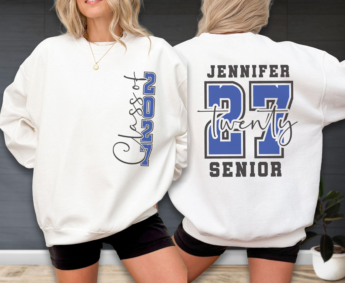 May include: A white crewneck sweatshirt featuring a graphic on the front that reads Class of 2027 in blue and black. The back of the sweatshirt displays the name Jennifer above the large blue number 27, with the word twenty and Senior below.