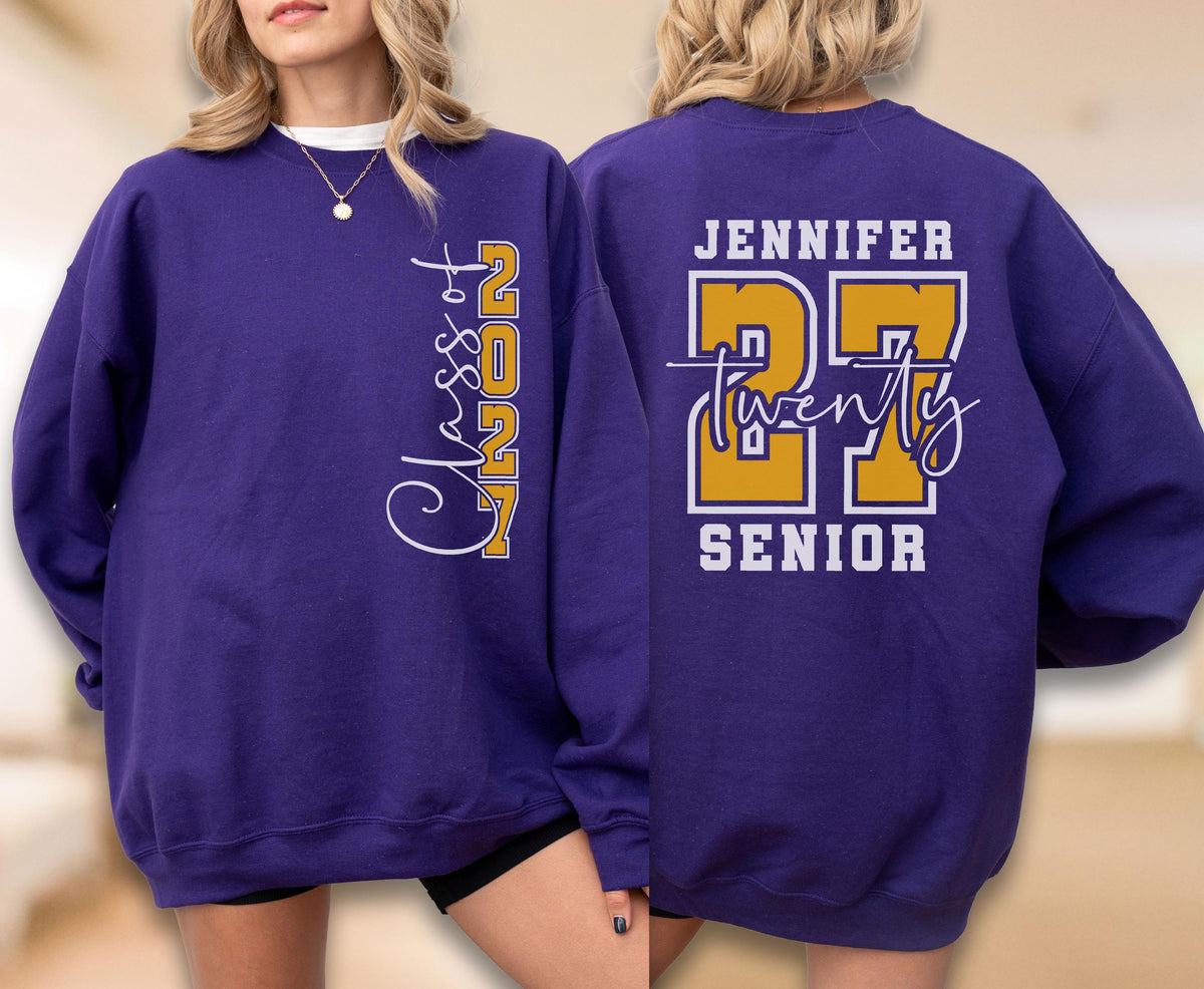 May include: A purple crewneck sweatshirt featuring white and gold graphics. The front displays vertical text reading Class of 2027. The back features the name Jennifer above the large gold number 27, the word twenty in script, and the word SENIOR.