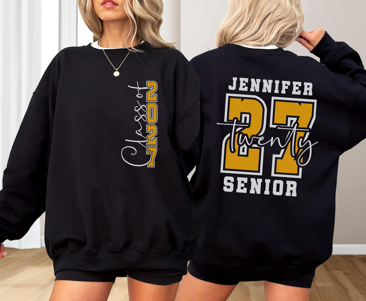 May include: A black crewneck sweatshirt featuring a vertical graphic on the front that reads Class of 2027 in white and gold. The back displays the name Jennifer above a large gold number 27, the word twenty in script, and the word SENIOR below.