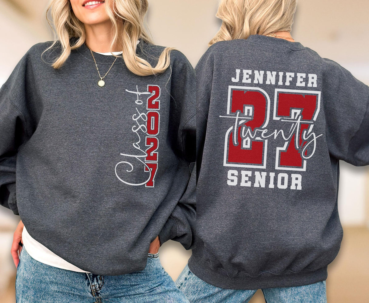 May include: A dark gray crewneck sweatshirt featuring white and red graphics. The front displays vertical text reading Class of 2027. The back features the name JENNIFER above the large red number 27, the word twenty in script, and SENIOR below.