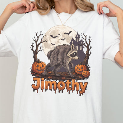 May include: A white t-shirt featuring a graphic of a raccoon walking in front of a full moon, a haunted house, bare trees, and three jack-o'-lanterns. The name Jimothy is printed in a dripping, orange, Halloween-themed font at the bottom.