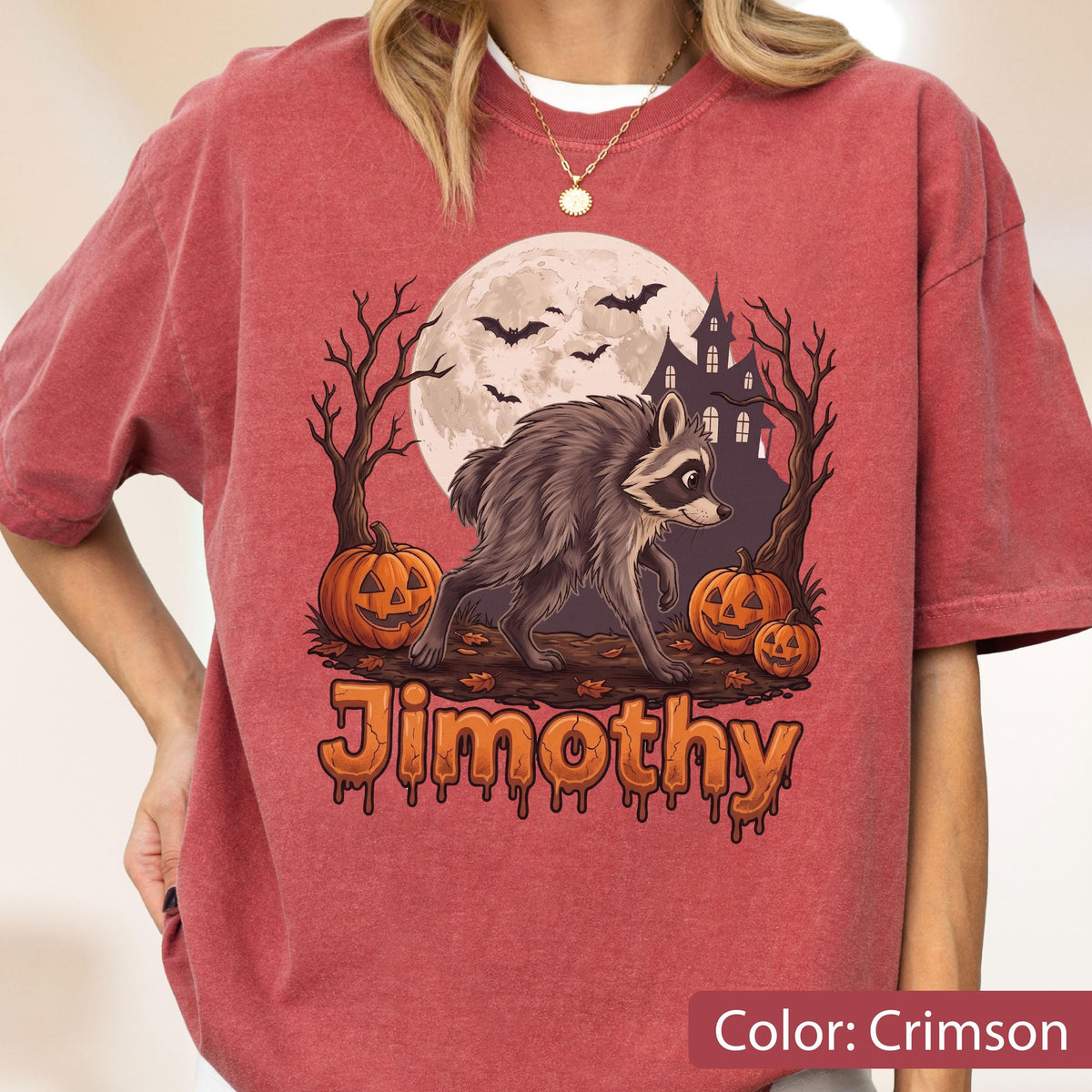 May include: A crimson short-sleeve t-shirt featuring a graphic of a raccoon walking in front of a full moon, a haunted house, bare trees, and jack-o'-lanterns. The text Jimothy is printed in an orange, dripping font below the illustration.