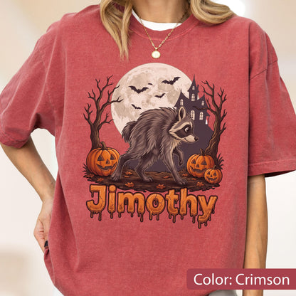 May include: A crimson short-sleeve t-shirt featuring a graphic of a raccoon walking in front of a full moon, a haunted house, bare trees, and jack-o'-lanterns. The text Jimothy is printed in an orange, dripping font below the illustration.