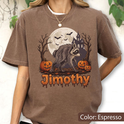 May include: An espresso-colored t-shirt featuring a graphic of a raccoon walking past two jack-o'-lanterns, a full moon, bats, and a haunted house silhouette. The name Jimothy is printed below the graphic in a dripping, orange-toned font.