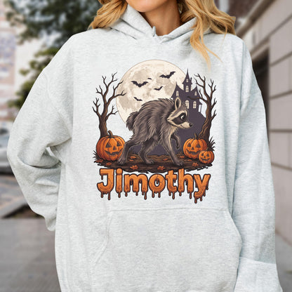 May include: A light gray hooded sweatshirt featuring a graphic of a raccoon walking in front of a full moon, a haunted house, bare trees, and three jack-o'-lanterns. The name Jimothy is printed below the graphic in orange, dripping-style letters.