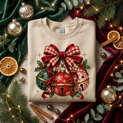 May include: A beige crewneck sweatshirt featuring a graphic of three jingle bells tied with a large red and white checkered bow. The central red bell has a snowflake pattern, the left is green, and the right is pink with a leopard print pattern.