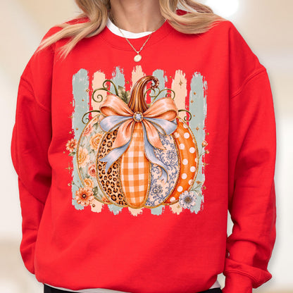 May include: A bright red crewneck sweatshirt featuring a large central graphic of a pumpkin decorated with various patterns including leopard print, orange gingham, floral motifs, and white polka dots, topped with a large light blue bow.