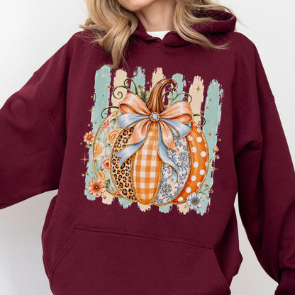 May include: A maroon hooded sweatshirt featuring a central graphic of a pumpkin decorated with various patterns including leopard print, orange gingham, floral motifs, and white polka dots, topped with a large light blue bow and green vines.