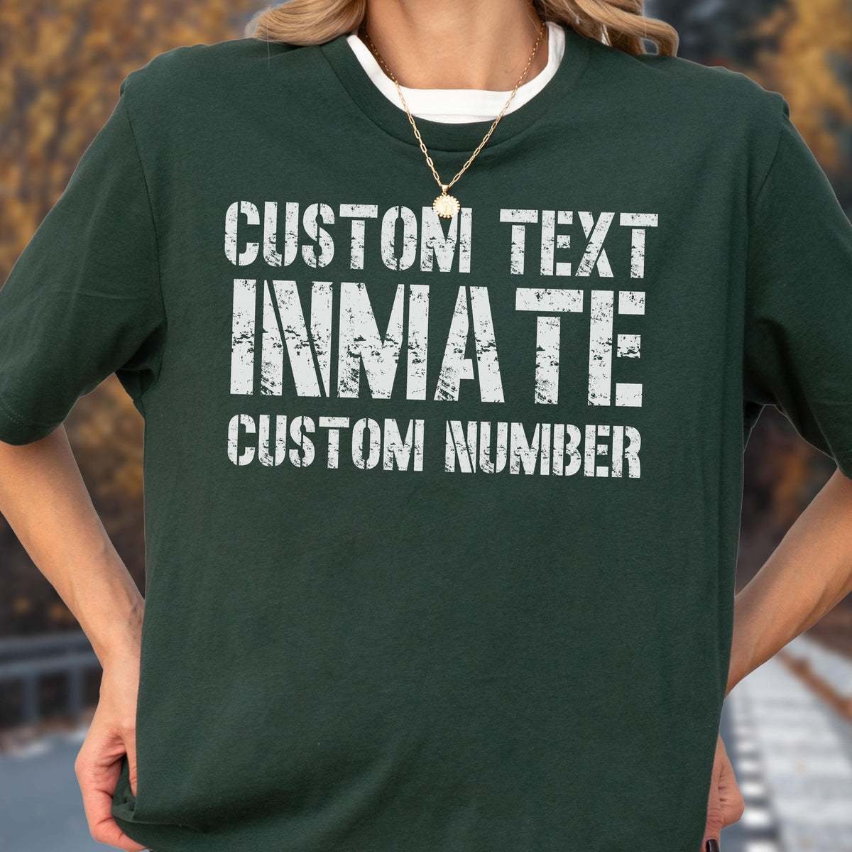 May include: A dark green short-sleeved t-shirt featuring white distressed-style text that reads CUSTOM TEXT, INMATE, and CUSTOM NUMBER. The shirt has a crew neckline and is worn over a white undershirt, with a gold-toned chain necklace visible.