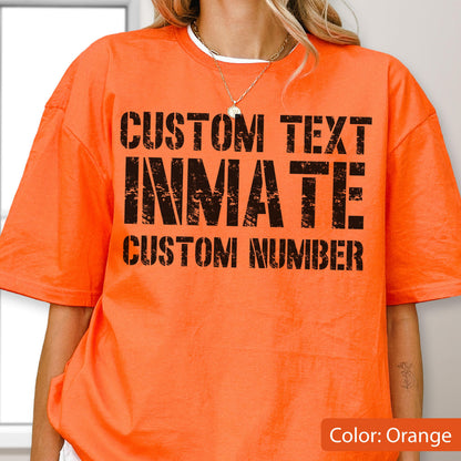 May include: A bright orange short-sleeved t-shirt featuring black distressed-style text printed on the front. The text reads CUSTOM TEXT, INMATE, and CUSTOM NUMBER in a bold, blocky font. The shirt has a crew neckline and a loose, relaxed fit.
