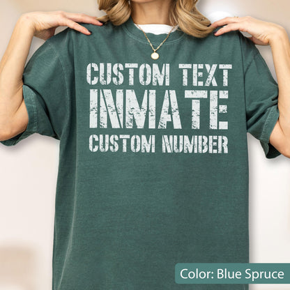 May include: A blue spruce colored short-sleeve t-shirt featuring white distressed-style text that reads CUSTOM TEXT INMATE CUSTOM NUMBER. The garment has a crew neckline and a relaxed fit, showcasing a weathered graphic design on the front chest area.