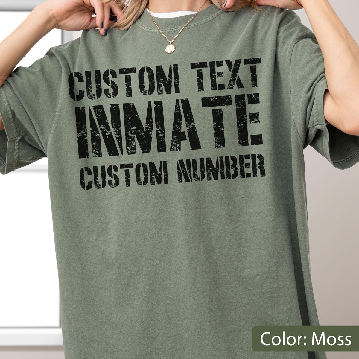 May include: A moss green short-sleeve t-shirt featuring black distressed-style text printed on the front. The text reads CUSTOM TEXT, INMATE, and CUSTOM NUMBER in a bold, blocky font. The shirt has a crew neckline and a relaxed, loose fit.