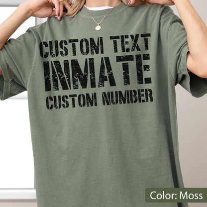 May include: A moss green short-sleeve t-shirt featuring black distressed-style text printed on the front. The text reads CUSTOM TEXT, INMATE, and CUSTOM NUMBER in a bold, blocky font. The shirt has a crew neckline and a relaxed, loose fit.