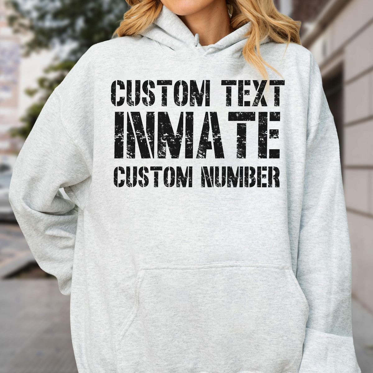 May include: A light gray hooded sweatshirt featuring black distressed-style text on the front. The text reads CUSTOM TEXT, INMATE, and CUSTOM NUMBER in a bold, block font. The garment includes a hood with drawstrings and a front kangaroo pocket.