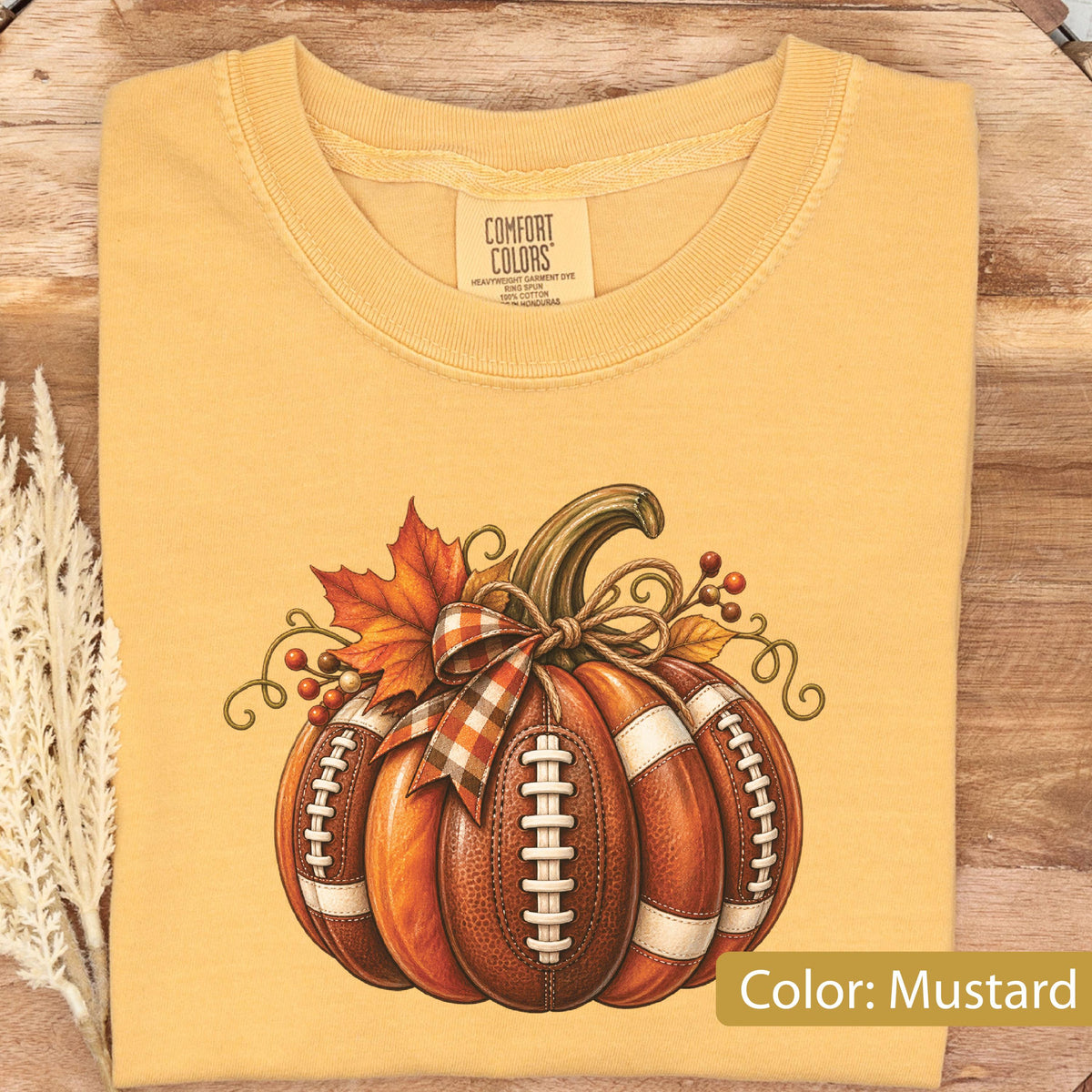 May include: A mustard yellow t-shirt featuring a graphic of a pumpkin designed with the texture and white laces of a football. The pumpkin is decorated with a plaid bow, an orange maple leaf, and small red berries, with the Comfort Colors brand label.