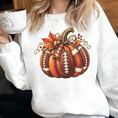 May include: A white crewneck sweatshirt featuring a central graphic of a pumpkin designed with the texture and white laces of an American football. The pumpkin is decorated with a plaid ribbon, orange maple leaves, and small red berries.